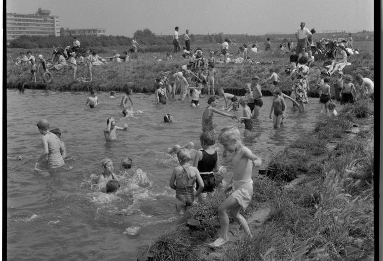 Tijdelijke recreatie bij de Alblashaven in de Spaanse Polder. Kinderen zwemmen in het water, op de kade liggen mensen in het gras te zonnen. Links de achterzijde van de Van Nellefabriek.