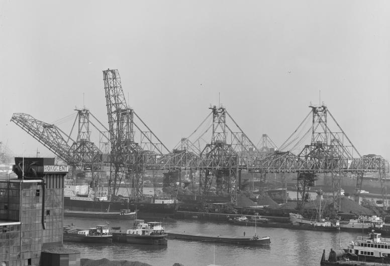 Binnenvaartschepen liggen in de Waalhaven bij de overslag van kolen. Op de voorgrond links het gebouw van de Rotterdamse Kolen Centrale (Rokocent). Op de achtergrond staan kranen op Pier 5.