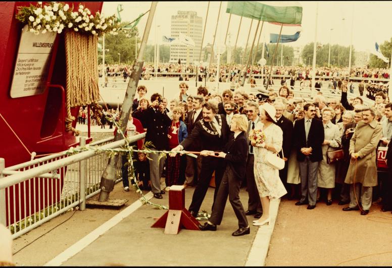 1 juli 1981: De opening van de Willemsbrug door Koningin Beatrix en prins Willem Alexander. Kroonprins Willem Alexander onthult op aanwijzing van burgemeester André van der Louw de gedenkplaquette. Hierbij werd een scheepshoorn in werking gesteld; dit sein werd door vele scheepshoorns en stoomfluiten overgenomen. Foto: Max van Essen. Collectie 4100, 1981-2303-kl
