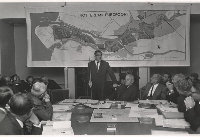28 juni 1966: In een vergadering van de wijkraad voor Hoek van Holland geeft burgemeester Thomassen uitleg over de uitbreidingsplannen van de Rotterdamse haven tussen Hoek van Holland en Maassluis. Vanuit het Westland werden grote bezwaren geuit tegen dit voornemen. Uiteindelijk komt het plan voor deze Rijnpoorthaven nooit tot uitvoering; dit besluit valt echter pas eind 1975. Fotograaf Robert Lantos, collectie 4282-XXXIII-1577-01-kl