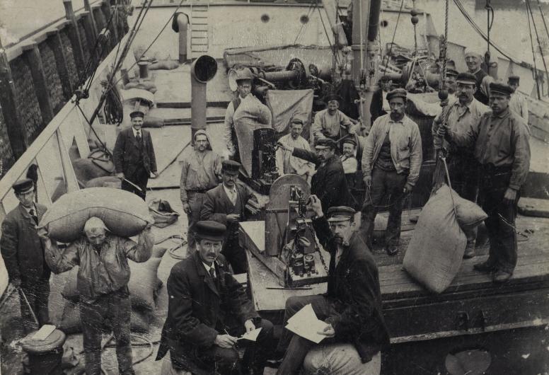  Havenarbeiders op een vrachtschip bezig met lossen van zakken graan. Op de voorgrond wegers en meters, links monsternemers. Collectie Vroege Foto's 4187_1975-427