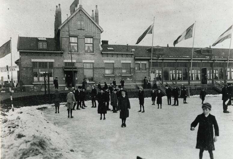 Schaatsers op de ijsbaan van ijsclub Kralingen aan de Kralingse Plaslaan Op de achtergrond het clubgebouw. Collectie 4202 XXIII-174a