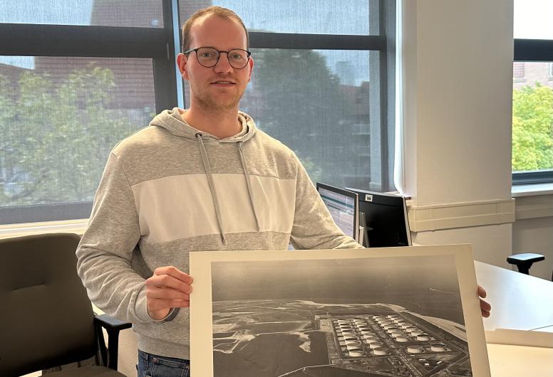 Daniël Vuijk op zijn werkplek. In zijn handen een luchtfoto van de Maasvlakte. 