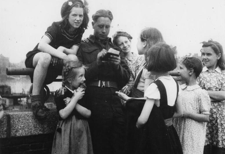 Een militair deelt handtekeningen uit aan meisjes [vermoedelijk aan de Boompjes bij de oprit naar de Willemburg], 10-05-1945 - 30-05-1945.