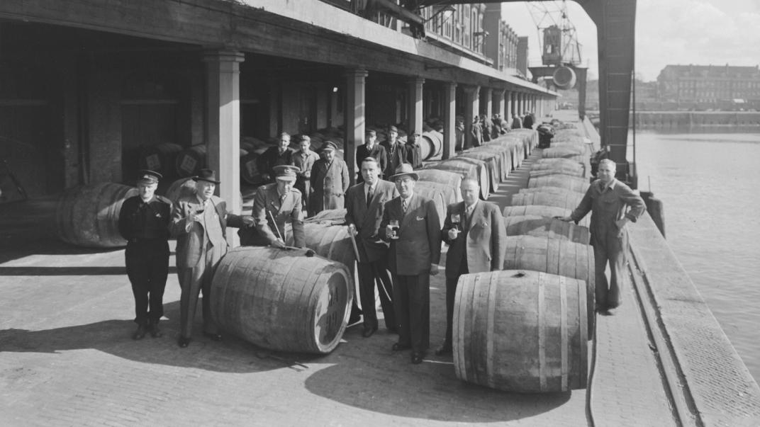 Cargadoors en douanebeambten bij vaten wijn op de kade bij het Gemeentelijk Entrepot, aan de Stieltjesstraat en Entrepôthaven, maart 1948